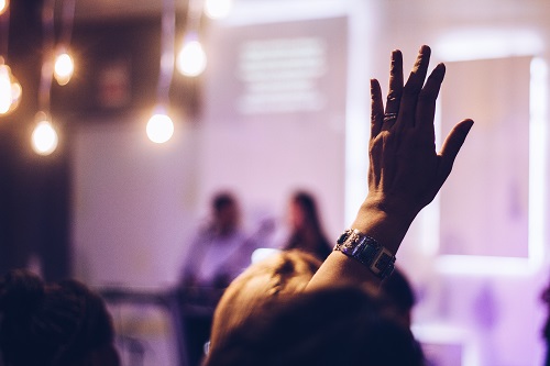 an image of a hand being raised in a large meeting